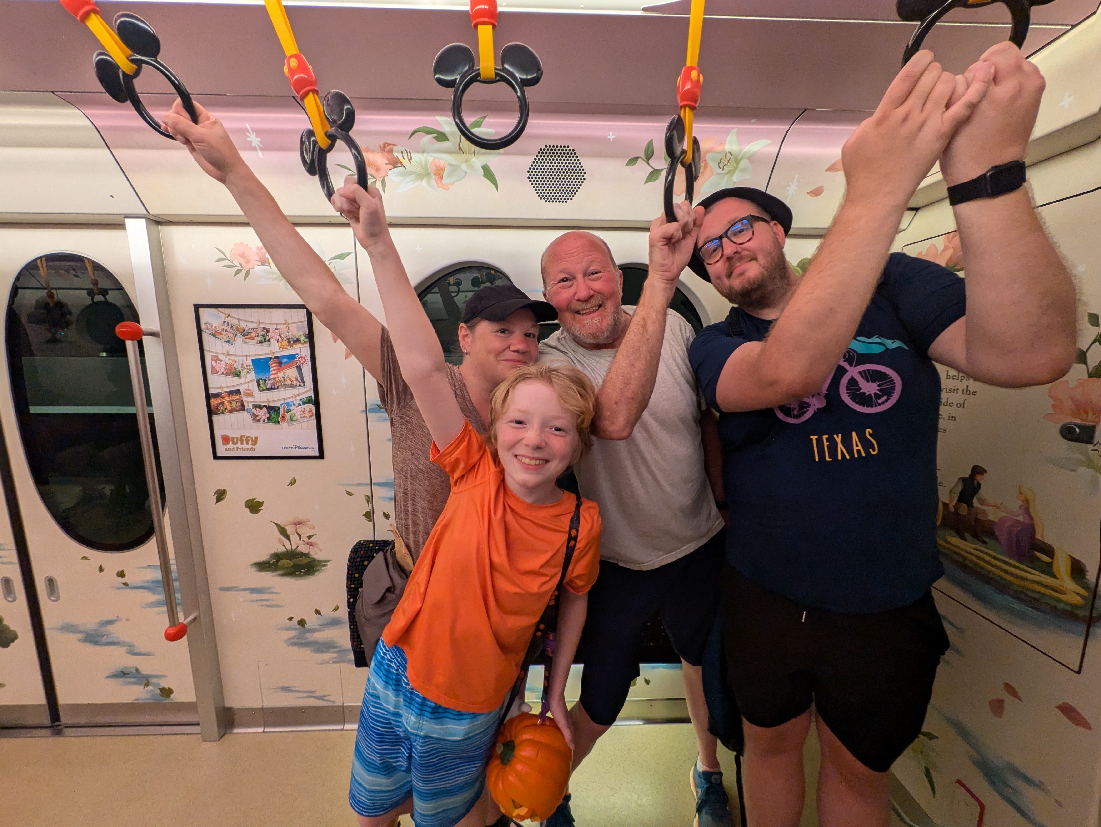 a family of five, a grandpa, a mom and her son and an uncle pose for a picture on a subway while holding the overhead straps.