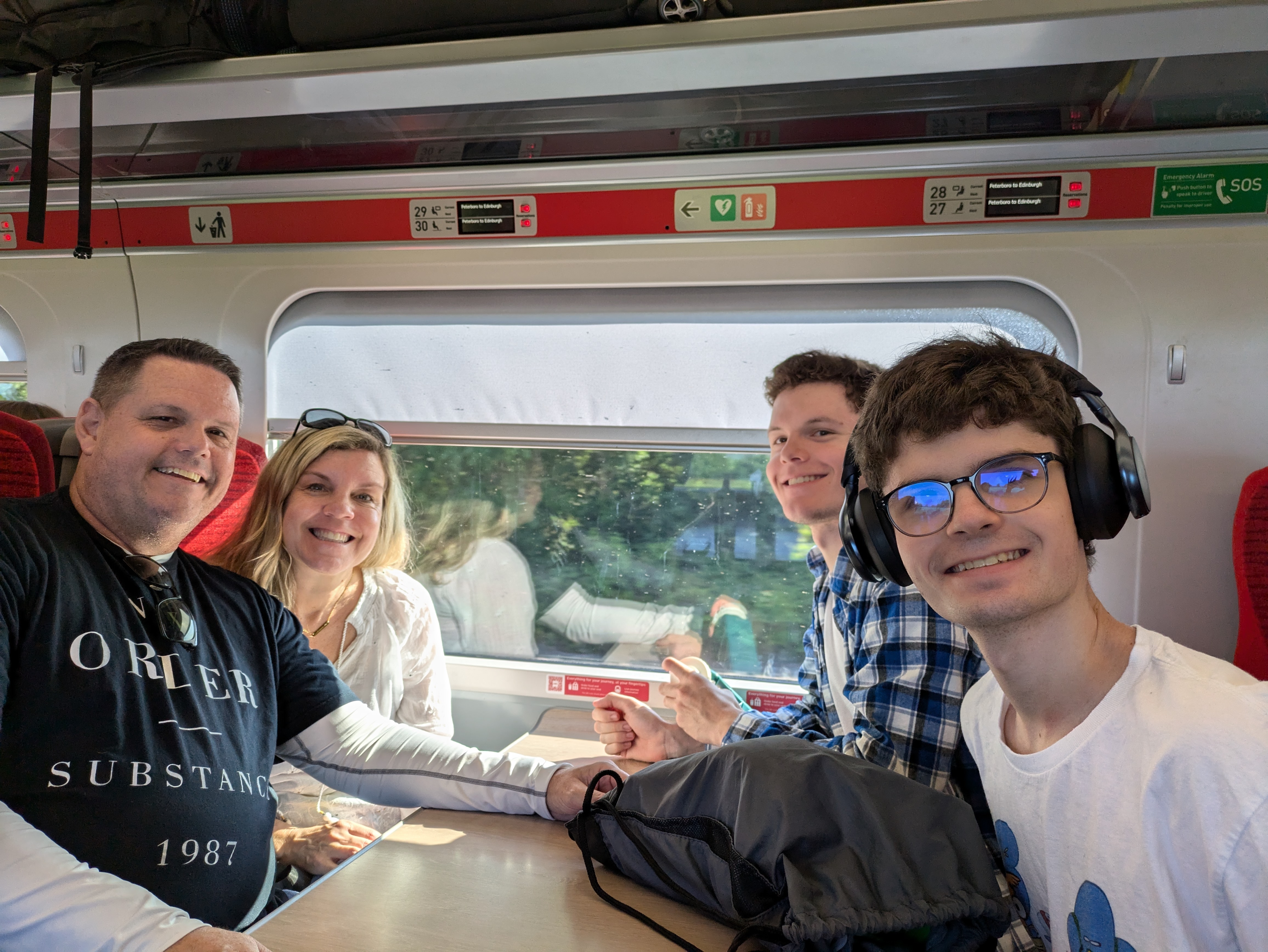 a family of four, a man, his wife and his two teenage sons smile for a picture while sitting at a table on a trainl